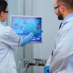 Scientist team arguing in front of computer looking at virus development in modern equipped laboratory. Multiethnic stuff analysing vaccine evolution using high tech for researching treatment.